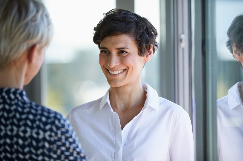 Portrait of smiling smiling businesswoman looking at colleague at the window in office